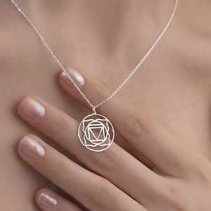Könnte beinhalten: Eine silberne Halskette mit einer zarten Kette und einem runden Anhänger mit einem geometrischen Design. Der Anhänger ist ein Symbol des Anahata-Chakras, des Herzchakras.