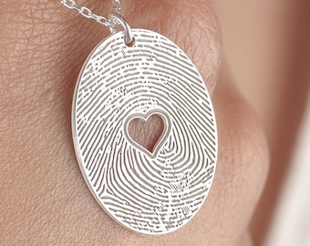 Puede incluir: Un collar de plata con un colgante con forma de huella dactilar con un corazón cortado en el centro.