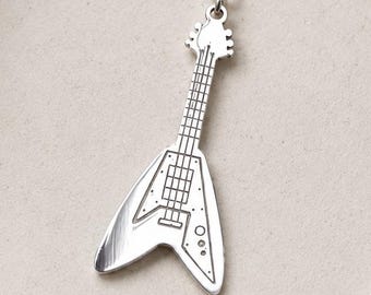 May include: A silver-toned metal pendant shaped like a V-style electric guitar, suspended from a matching delicate silver chain. The pendant features engraved details representing the fretboard, pickups, and bridge of the instrument.
