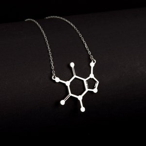 Puede incluir: Un collar de plata con un colgante con forma de la estructura química de la cafeína.