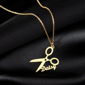 May include: Gold necklace with a pendant featuring a pair of scissors and the name "Daisy" written in cursive.
