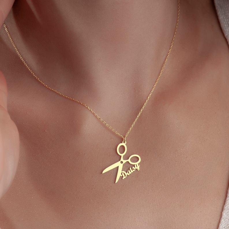 May include: Gold necklace with a scissor pendant and the name "Daisy" written inside the scissor blades.