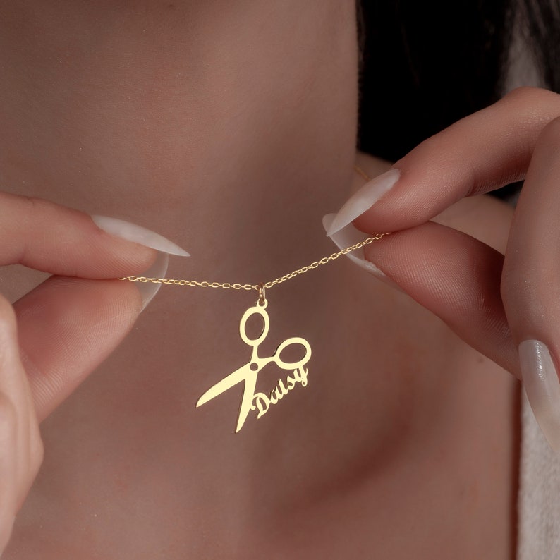 May include: Gold necklace with a scissor pendant and the name "Daisy" written on it.