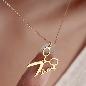 May include: Gold necklace with a pendant featuring a pair of scissors and the name "Daisy" written in cursive.