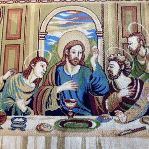 Może przedstawiać: Gobelin przedstawiający Ostatnią Wieczerzę, scenę z Biblii. Jezus siedzi w centrum stołu, otoczony przez swoich uczni&oacute;w. Gobelin jest tkany z misternymi detalami i żywymi kolorami, w tym odcieniami niebieskiego, zielonego, czerwonego i złotego.