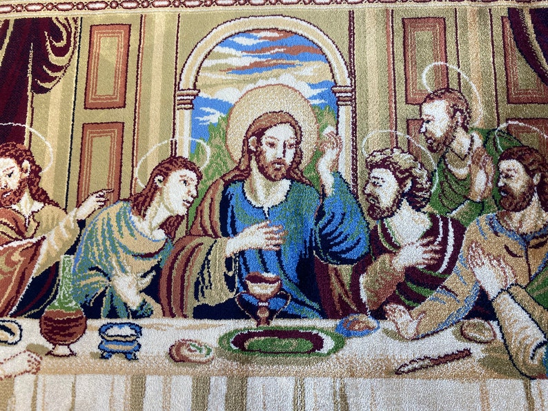 Może przedstawiać: Gobelin przedstawiający Ostatnią Wieczerzę, scenę z Biblii. Jezus siedzi w centrum stołu, otoczony przez swoich uczni&oacute;w. Gobelin jest tkany z misternymi detalami i żywymi kolorami, w tym odcieniami niebieskiego, zielonego, czerwonego i złotego.