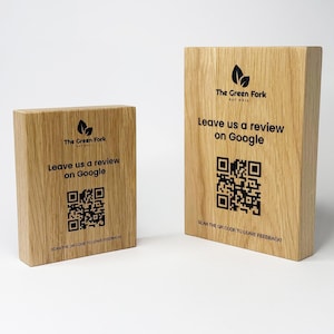 Puede incluir: Dos bloques de madera con el texto "The Green Fork" y "Leave us a review on Google" impresos en negro. Cada bloque tiene un código QR para comentarios. Los bloques son de madera clara.