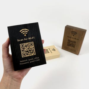 Può includere: Un blocco di legno nero con un simbolo Wi-Fi e la scritta "Scan for Wi-Fi". Sotto c'è un codice QR e informazioni sulla rete. Due blocchi di legno aggiuntivi sono sullo sfondo, uno nero e uno marrone chiaro.