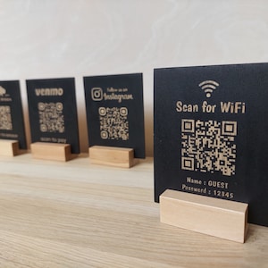 May include: Four black square signs with QR codes and text on them. The signs are on wooden stands. The text on the signs reads "Black Bison", "Venmo Scan to Pay", "Follow us on Instagram", and "Scan for WiFi Name: GUEST Password: 12345".