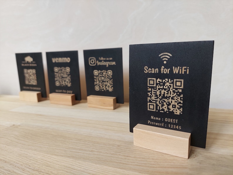 May include: Four black square signs with QR codes and text on them. The signs are on wooden stands. The text on the signs reads "Black Bison", "Venmo Scan to Pay", "Follow us on Instagram", and "Scan for WiFi Name: GUEST Password: 12345".