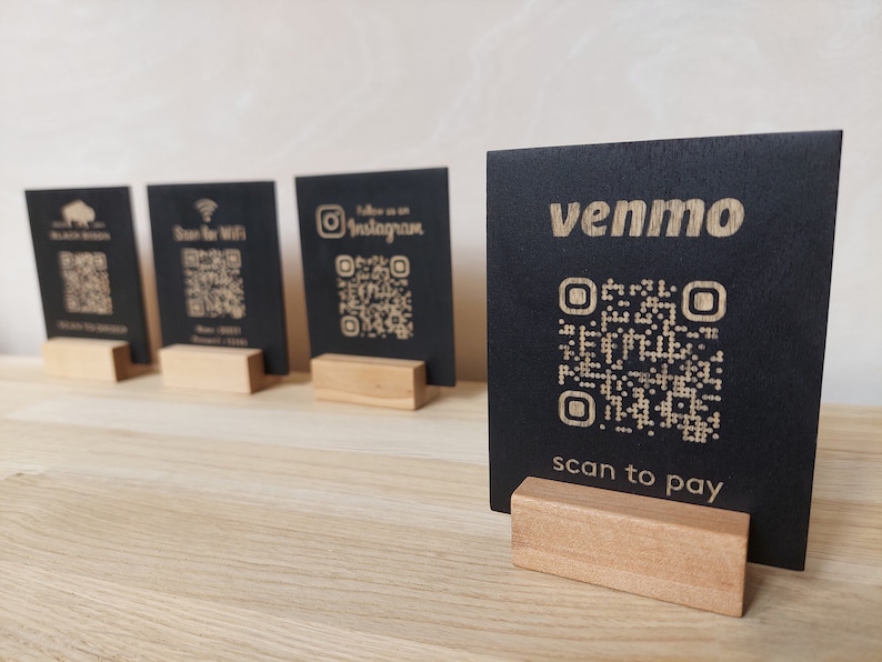May include: Five black square signs with QR codes and text on them. The signs are on wooden stands. The text on the signs reads "Black Bison", "Scan for Wifi", "Follow us on Instagram", "venmo", and "scan to pay".