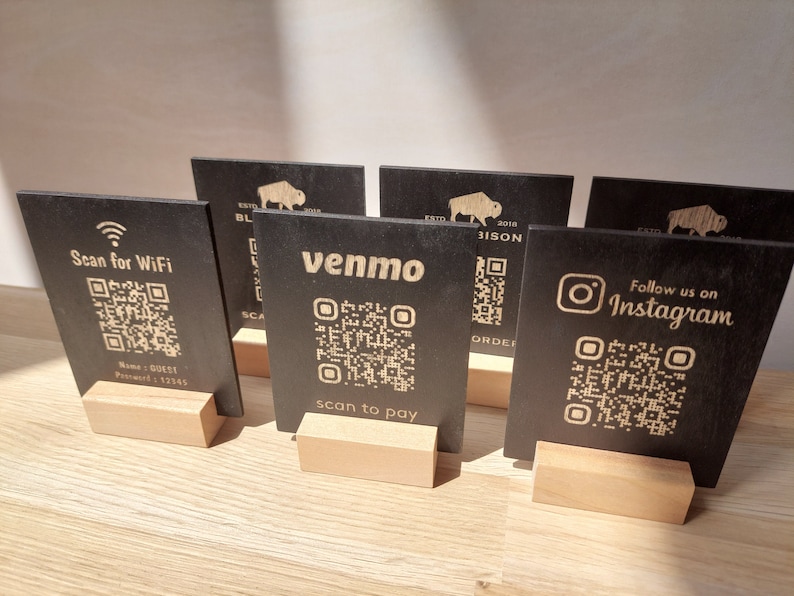 May include: Five black wooden signs with QR codes and text. The signs are on wooden stands. The text on the signs reads: "Scan for WiFi", "venmo", "Follow us on Instagram", "ESTD 2018 BL BISON", and "ESTD 2018 BISON".
