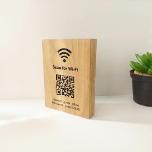 Pode incluir: Uma placa de Wi-Fi de madeira com um código QR e o texto "Scan for Wi-Fi". A placa também exibe o nome da rede e a senha. À direita da placa, há uma pequena suculenta em vaso.