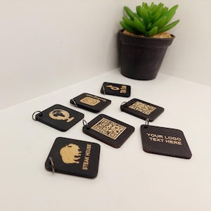 May include: A set of eight black wooden keychains with gold engraved designs. The designs include a globe, a QR code, a TikTok logo, an Instagram logo, a buffalo, and the text "Steak House". One keychain has the text "Your Logo Text Here".