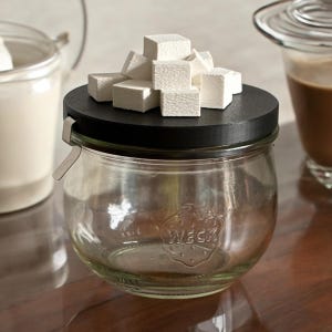 May include: A glass jar with a black lid and a silver clasp. The jar is filled with white sugar cubes. The jar has the word "WECK" embossed on the side.