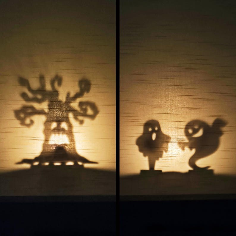 May include: Halloween-themed shadow art featuring a spooky tree and two playful ghost figures. The silhouettes are cast against a warm, textured background, creating a festive and eerie ambiance. Perfect for Halloween decor.