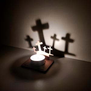May include: A wooden candle holder with a tea light candle, casting cross-shaped shadows on the wall. The holder features several small wooden crosses. The warm light of the candle creates a peaceful and spiritual ambiance.