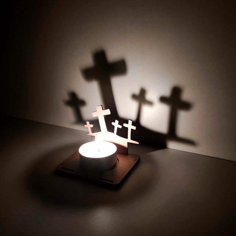 May include: A wooden candle holder with a tea light candle, casting cross-shaped shadows on the wall. The holder features several small wooden crosses. The warm light of the candle creates a peaceful and spiritual ambiance.