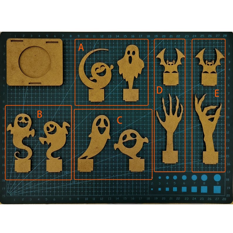 May include: A collection of laser-cut wooden Halloween decorations, including ghosts, bats, and spooky hands. The pieces are arranged on a grid cutting mat, ready for assembly or painting. The designs are perfect for DIY Halloween crafts.