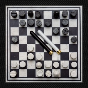 Puede incluir: Un juego de damas de m&aacute;rmol blanco y negro con fichas blancas y negras. Dos fichas negras y doradas est&aacute;n en el tablero.