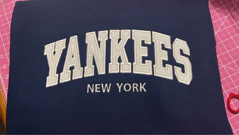 May include: A navy blue fabric patch with white embroidered text that reads "YANKEES NEW YORK".