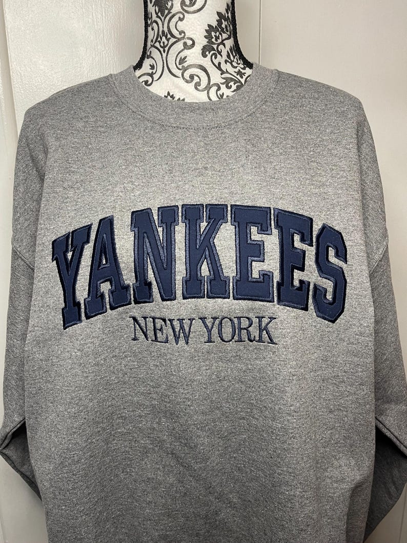 May include: Gray sweatshirt with a navy blue embroidered New York Yankees logo.