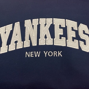 May include: A navy blue sweatshirt with white embroidered text that reads "YANKEES NEW YORK".