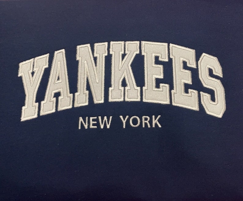 May include: A navy blue sweatshirt with white embroidered text that reads "YANKEES NEW YORK".