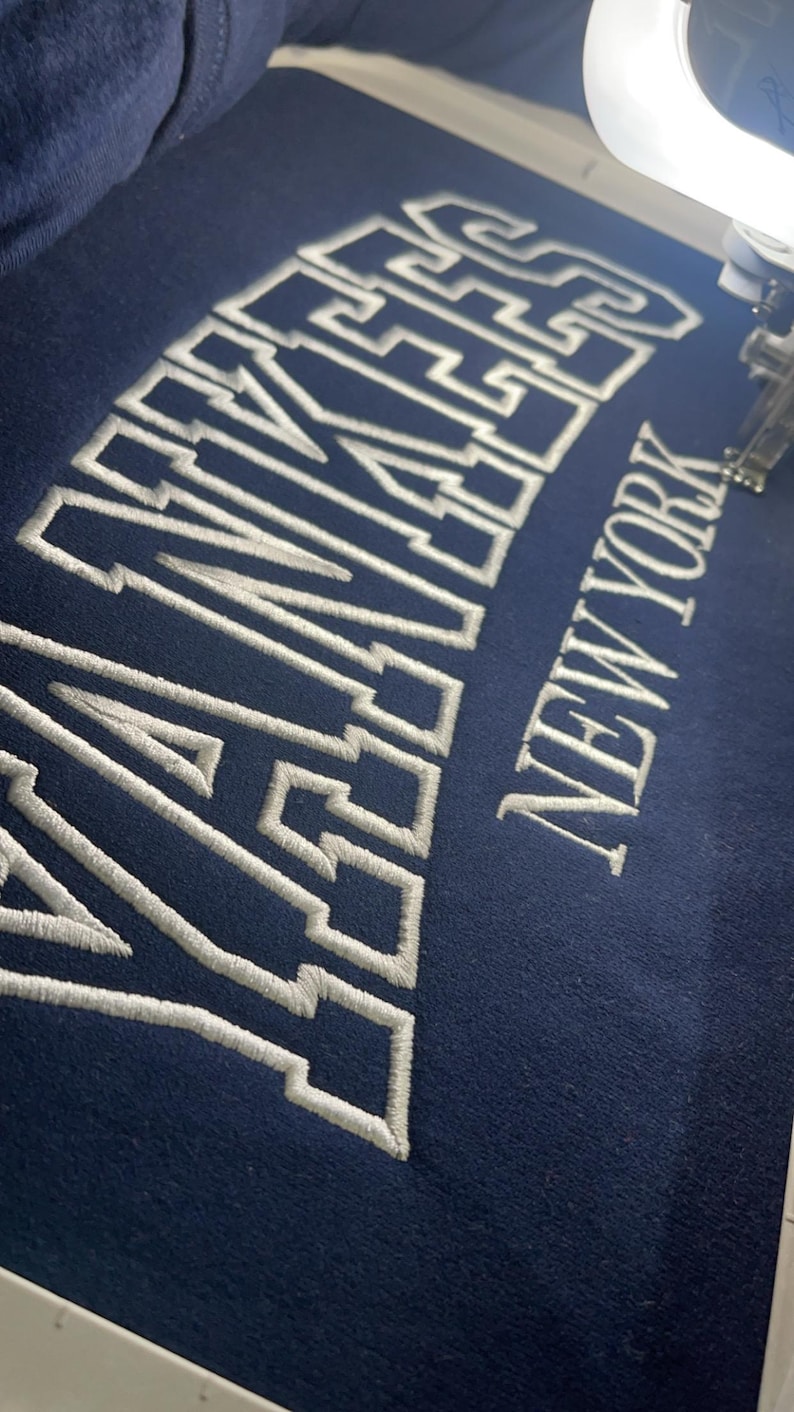 May include: A navy blue sweatshirt with white embroidered lettering that reads "YANKEES NEW YORK".