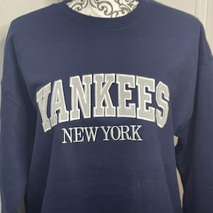 May include: A navy blue sweatshirt with the words "YANKEES NEW YORK" embroidered in silver on the front.