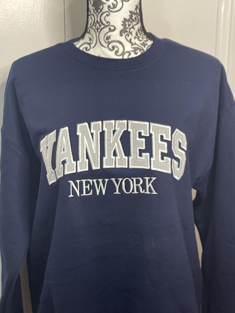 May include: A navy blue sweatshirt with the words "YANKEES NEW YORK" embroidered in silver on the front.