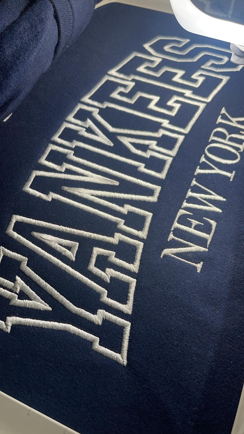 May include: A navy blue sweatshirt with white embroidered lettering that reads "YANKEES NEW YORK".
