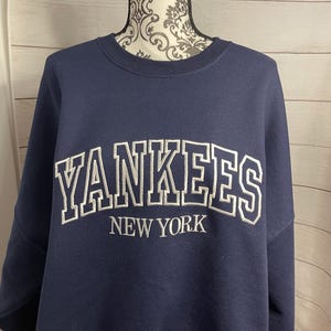 May include: A navy blue sweatshirt with a white embroidered "YANKEES NEW YORK" logo.