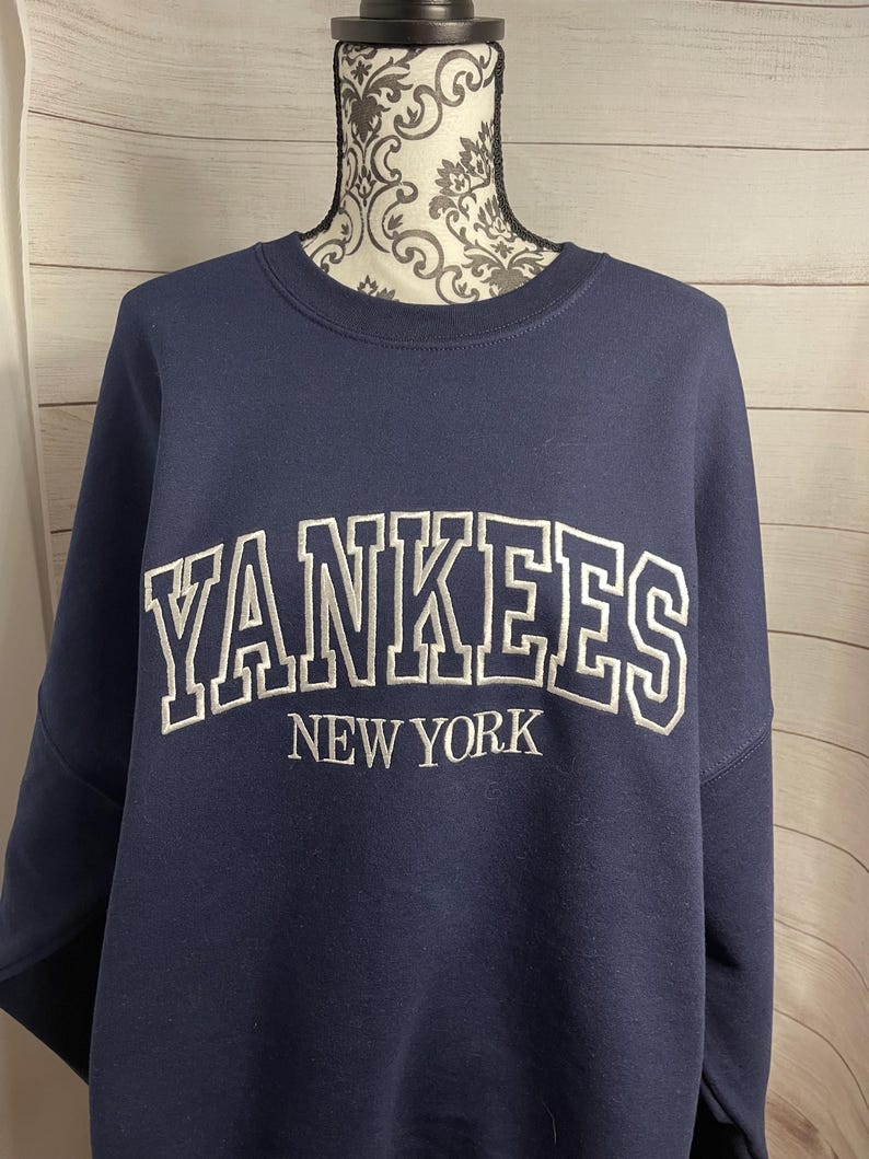 May include: A navy blue sweatshirt with a white embroidered "YANKEES NEW YORK" logo.