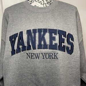 May include: Gray sweatshirt with a navy blue embroidered "YANKEES NEW YORK" logo.