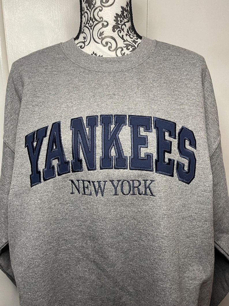 May include: Gray sweatshirt with a navy blue embroidered "YANKEES NEW YORK" logo.