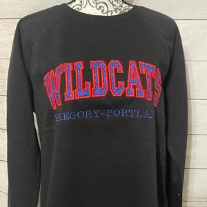 May include: Black sweatshirt with the word "WILDCATS" in red and blue glitter lettering with a blue outline. The text "GREGORY-PORTLAND" is in blue lettering below the word "WILDCATS".