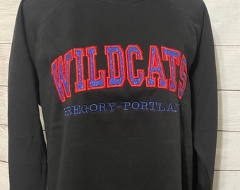 May include: Black sweatshirt with the word "WILDCATS" in red and blue glitter lettering with a blue outline. The text "GREGORY-PORTLAND" is in blue lettering below the word "WILDCATS".