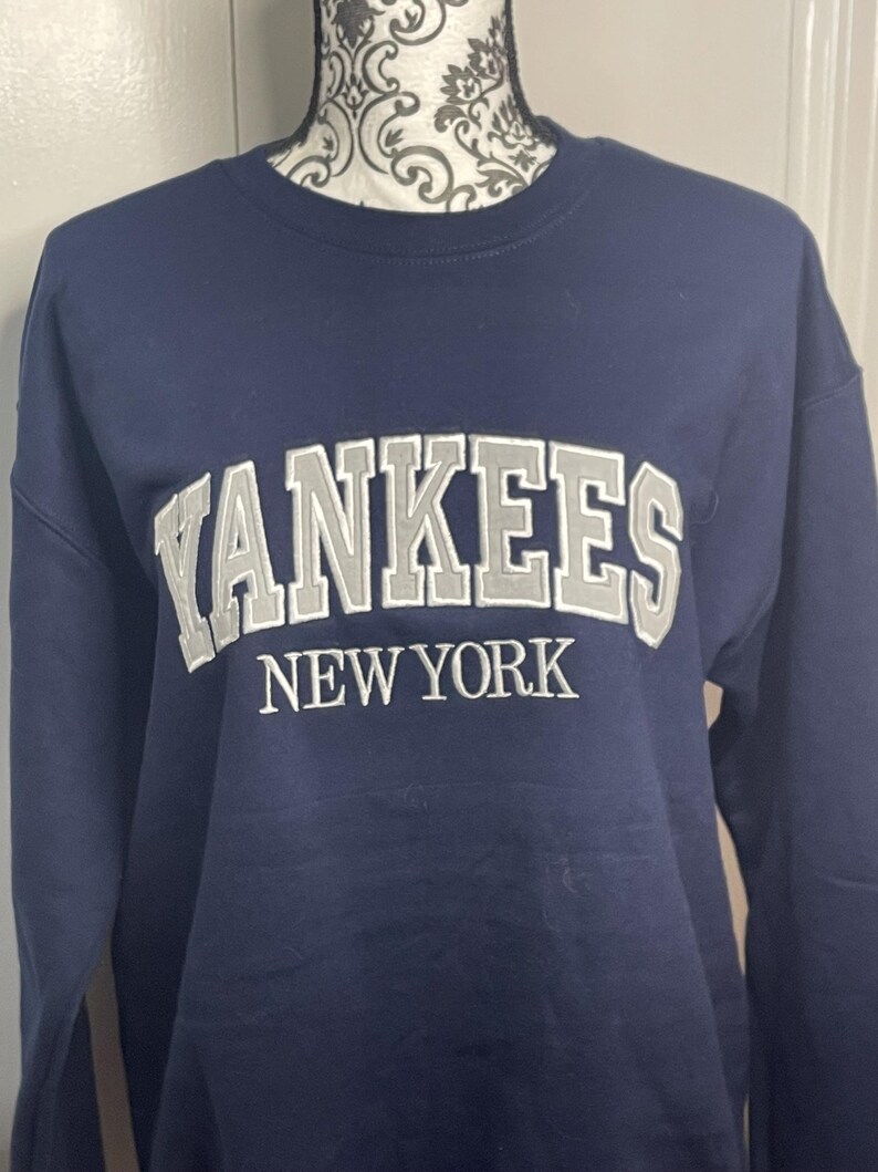 May include: A navy blue sweatshirt with the words "Yankees New York" embroidered in white on the front.