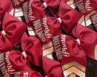 May include: A set of maroon cheer bows with white and silver glitter accents. Each bow has the text "SINTON Pirates" written on it.