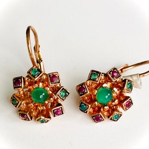 Puede incluir: Un par de pendientes de tono dorado con un diseño floral. Los pendientes presentan una piedra verde en el centro rodeada de piedras rojas y verdes más pequeñas.