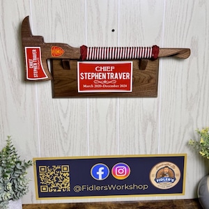 Puede incluir: Un hacha de bombero de madera con un mango de cuerda rojo y blanco. El hacha está montada en una placa de madera con una placa roja que dice "Jefe Stephen Traver Marzo 2020-Diciembre 2024".