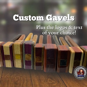 Op de afbeelding: Een rij op maat gemaakte houten hamerhamer met verschillende houtnerfpatronen en kleuren. De hamerhamer zijn in een rij op een houten oppervlak gerangschikt. De tekst "Custom Gavels" en "Plus the logos & text of your choice!" wordt boven de hamerhamer weergegeven. Een cirkelvormig logo met de tekst "Handcrafted by" en het gezicht van een persoon wordt onder de hamerhamer weergegeven.