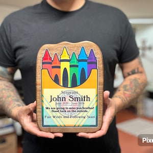 Puede incluir: Una placa de madera con un diseño de caja de crayones de colores. La placa dice "Sergeant John Smith Junio 2020 - Junio 2024" y "We are going to miss you brother! Good luck on the outside. Fair Winds and Following Seas!"