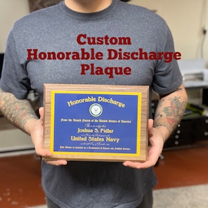 Puede incluir: Una placa de madera con un borde azul y dorado, que honra la baja honorable de una persona de la Marina de los Estados Unidos. La placa dice "Honorable Discharge" y "From the Armed Forces of the United States of America". El texto también incluye el nombre "Joshua S. Fidler" y "United States Navy".