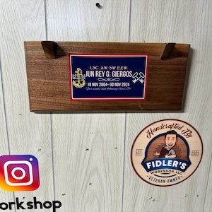 May include: A rectangular wooden plaque featuring a blue and red commemorative plate with the text LSC AW SW EXW JUN REY G. GIERGOS 18 NOV 2004-30 NOV 2024 Your winds and following seas, Go. The plaque includes a USN anchor emblem and crossed keys.