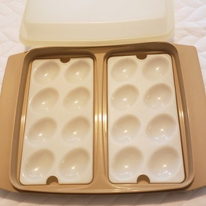 May include: A beige plastic egg holder with a clear lid. The holder has two sections, each with six egg-shaped depressions.