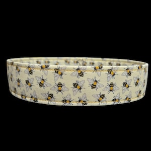 Peut inclure: Un collier pour chien en tissu avec un motif répété d'abeilles noires et jaunes sur un fond jaune clair. Le collier est en forme de bande, avec un bord cousu.