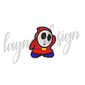 May include: An embroidered patch featuring a red hooded character with a white oval mask, two black oval eye holes, a small black mouth, a yellow belt buckle, and blue shoes. The design is outlined in black thread with a visible stitch texture.