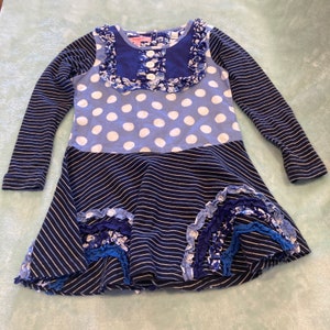 May include: A blue and white polka dot dress with a navy blue striped skirt and ruffle trim. The dress has long sleeves and a round neckline.